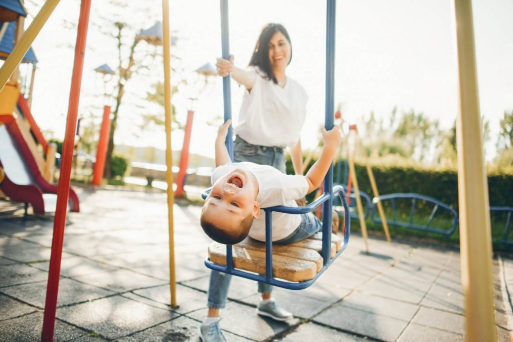 Anak bermain ayunan di taman dengan pengawasan orang tua, menyoroti pentingnya keselamatan