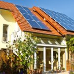 Rumah modern dengan panel surya di atap, dikelilingi taman hijau, memanfaatkan energi matahari untuk kebutuhan listrik